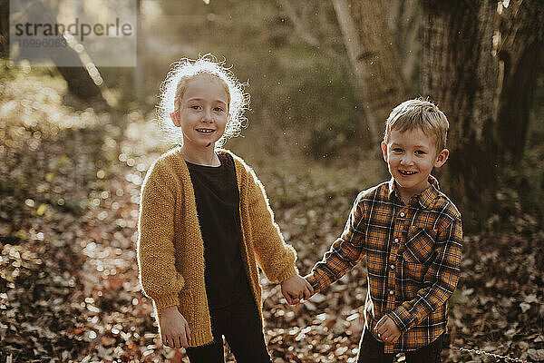 Bruder und Schwester lächelnd und händchenhaltend im Wald stehend