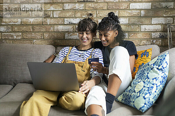 Lächelndes lesbisches Paar beim Online-Shopping  während es zu Hause sitzt