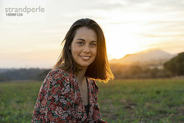 Lächelnde junge Frau gegen den Himmel bei Sonnenuntergang