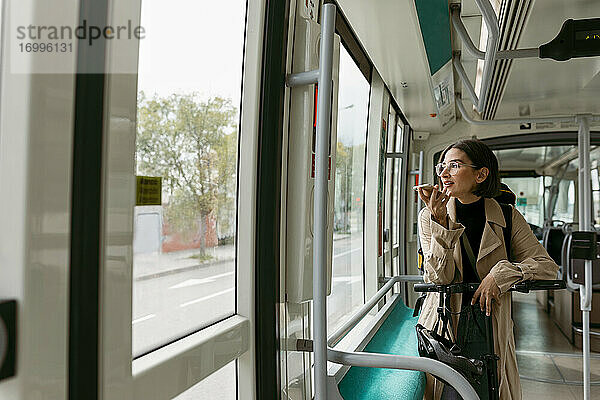 Frau mit Elektroroller schaut weg  während sie in der Straßenbahn mit dem Handy telefoniert