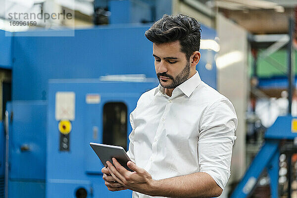 Männlicher Unternehmer  der ein digitales Tablet benutzt  während er in einer Fabrik steht