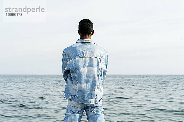 Junger Mann im Jeansanzug steht am Meer