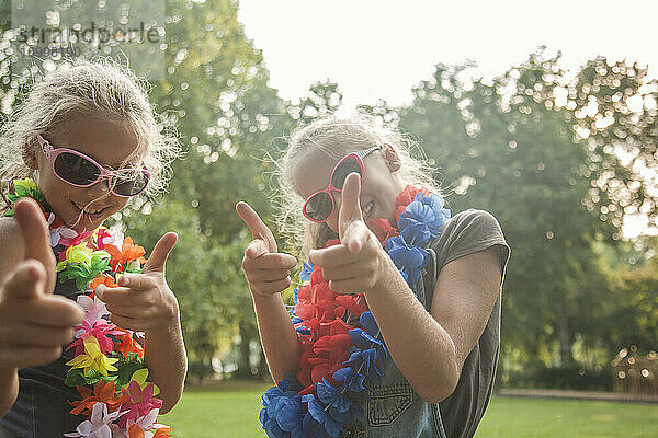 Fröhliche Mädchen mit Sonnenbrillen und Blumengirlanden in einem öffentlichen Park