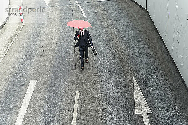 Geschäftsmann mit Regenschirm geht auf Straße mit Pfeil Zeichen