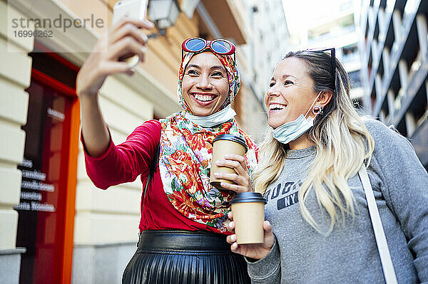 Freundinnen machen ein Selfie mit Kaffeetassen in der Stadt während der COVID-19
