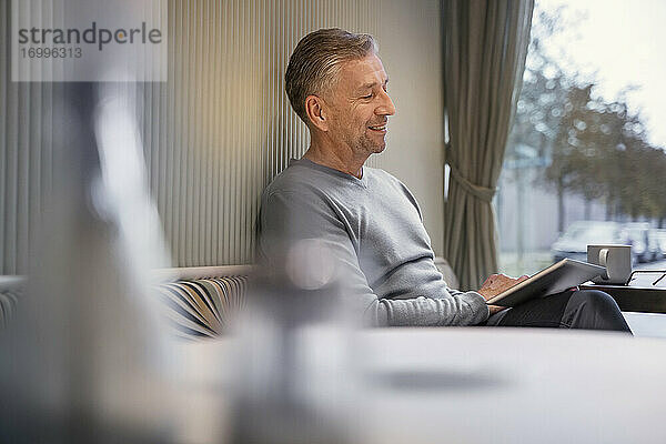 Lächelnder Geschäftsmann  der ein digitales Tablet benutzt  während er in einem modernen Cafe sitzt