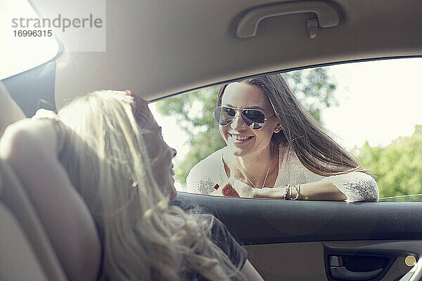 Junge Frau lehnt sich an ein Autofenster und spricht mit einem Freund während einer Autofahrt