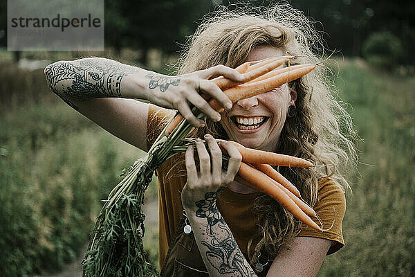 Bäuerin lächelt und hält Karotten auf dem Bauernhof