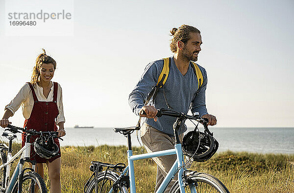 Lächelnder Mann und Frau mit Fahrrädern  die gegen einen klaren Himmel laufen