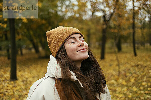 Lächelnde junge Frau mit geschlossenen Augen im herbstlichen Park