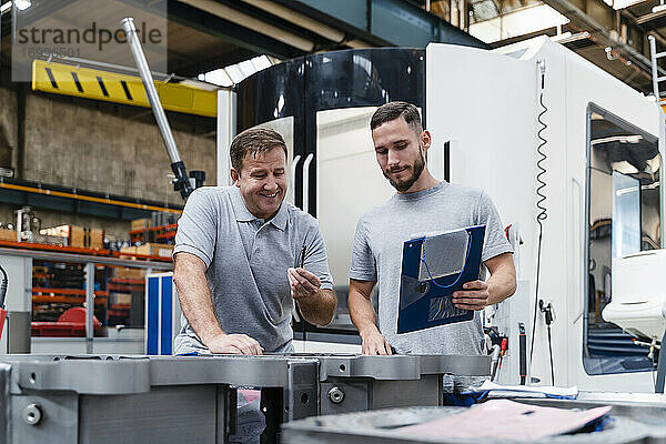 Reifer männlicher Techniker  der ein Produkt analysiert  neben einem jungen Kollegen in einer industriellen Fabrik