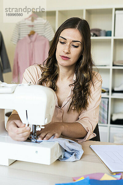 Junge Designerin an der Nähmaschine sitzend im Atelier