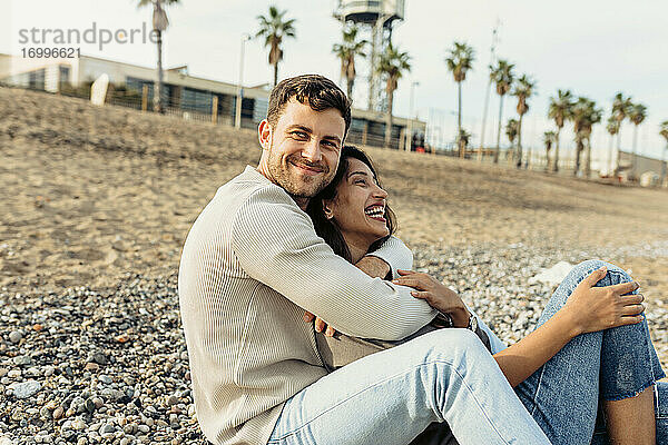 Junges Paar lacht  während sie sich am Strand umarmen