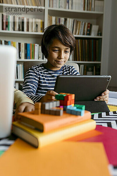 Lächelnder Junge mit digitalem Tablet am Tisch
