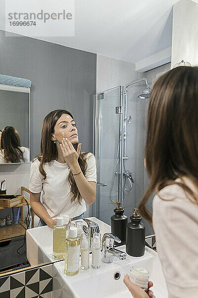 Frau beim Auftragen von Gesichtscreme im Badezimmer zu Hause