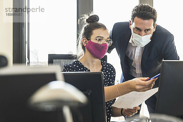 Geschäftsleute mit Gesichtsmaske diskutieren bei der Arbeit im Büro