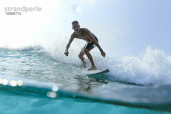 Mann mit Surfbrett surft auf Meereswelle gegen klaren Himmel