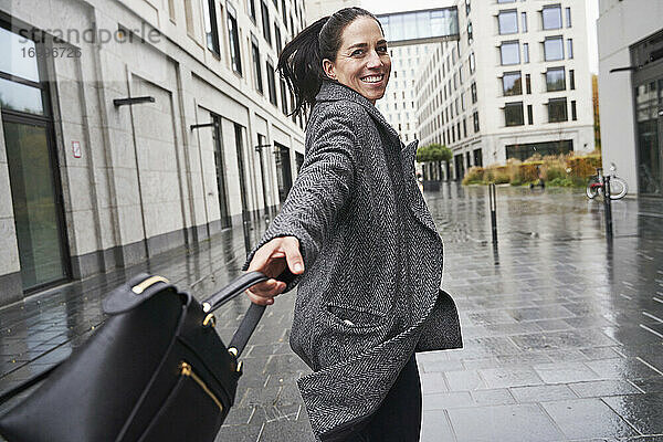 Glückliche Geschäftsfrau  die beim Gehen auf dem Fußweg ihre Handtasche dreht