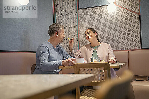 Lächelnde Geschäftsfrau füttert Mann  während sie in einem modernen Café sitzt