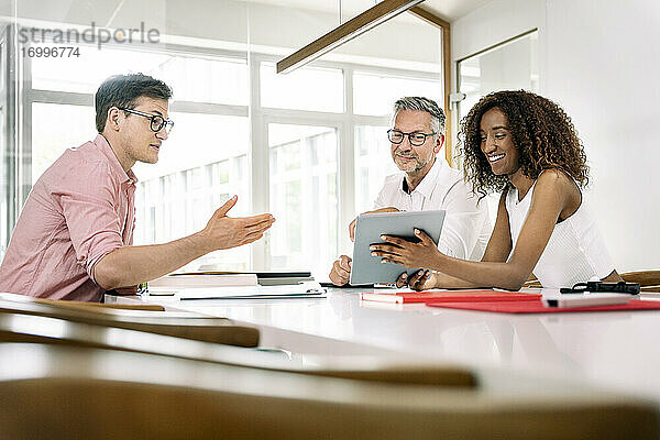 Eine lächelnde Geschäftsfrau zeigt ihren Kollegen während einer Besprechung im Büro ein digitales Tablet