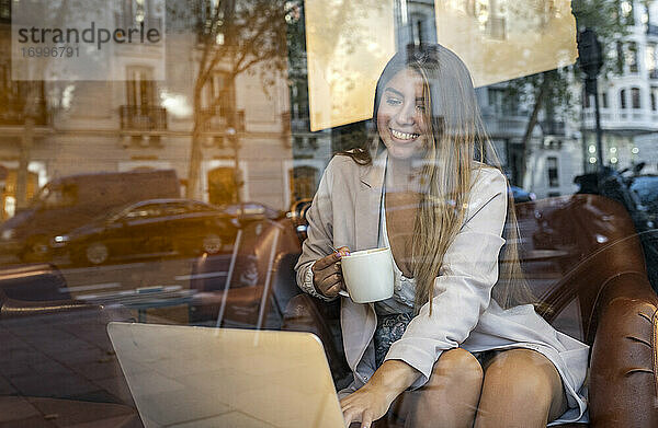 Lächelnde Frau  die einen Laptop benutzt  während sie in einem Café Kaffee trinkt