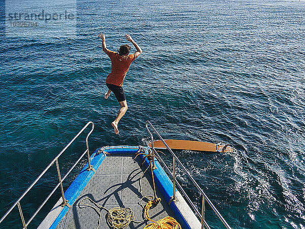 Abenteuerlustiger Mann  der an einem sonnigen Tag vom Bootsdeck springt  um zu surfen