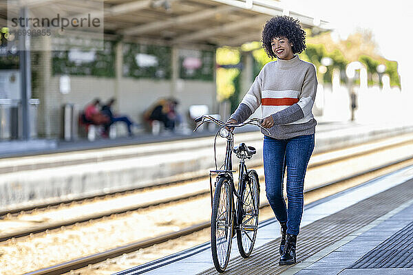 Junge Frau geht mit dem Fahrrad am Bahnsteig spazieren und träumt vor sich hin