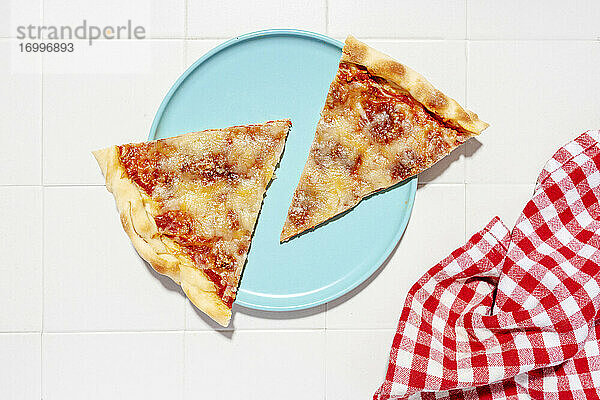 Zwei Scheiben Pizza Margherita auf blauem Teller und rot-karierter Serviette