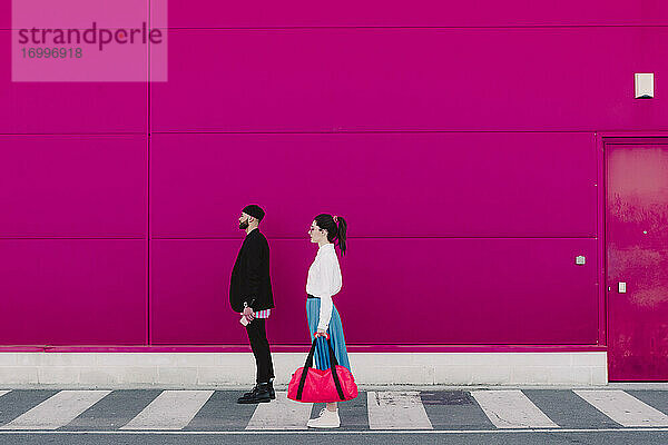 Mann und Frau stehen auf einer rosa Wand und schauen weg