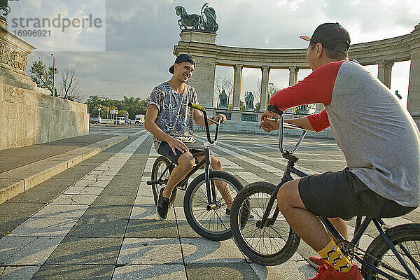 Junge männliche BMX-Fahrer  die auf Fahrrädern sitzend auf dem Heldenplatz eine Pause machen  Budapest  Ungarn