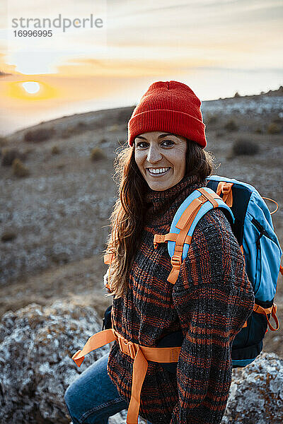 Glückliche Wanderin mit Rucksack auf einem Berg stehend bei Sonnenuntergang