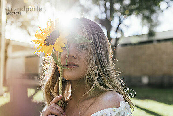 Junge Frau bedeckt ihr Gesicht mit Sonnenblumen im Hinterhof