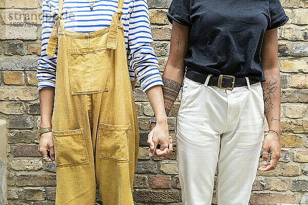 Junges lesbisches Paar hält sich an den Händen  während es an einer Mauer steht