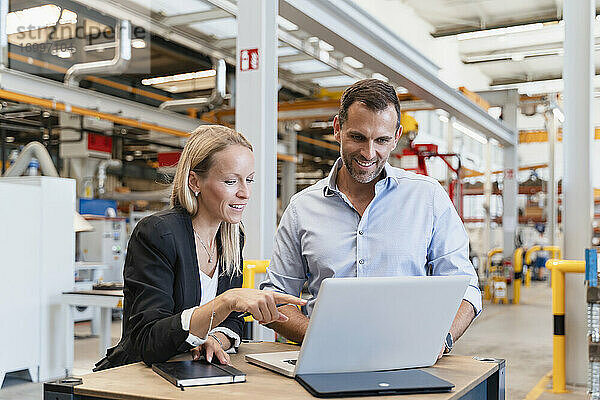 Lächelnder Geschäftsmann und Unternehmerin mit Laptop in einer Fabrik
