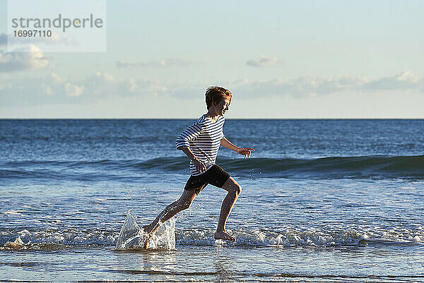 Lächelnder Junge läuft im Wasser am Strand