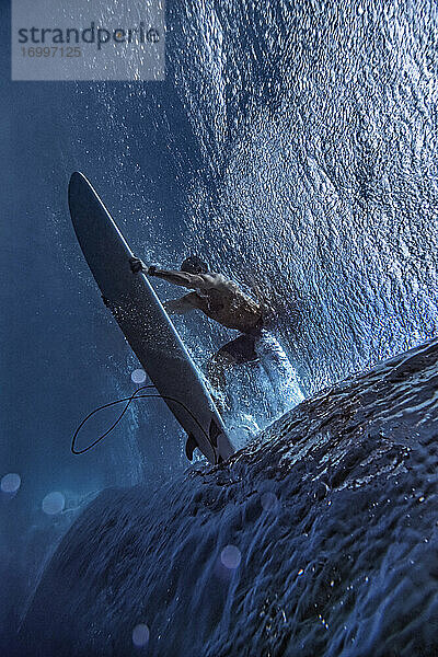 Männlicher Surfer surft auf einem Surfbrett unter Wasser auf den Malediven