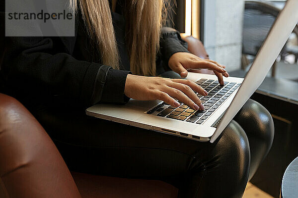 Junge Frau tippt auf einem Laptop  während sie im Cafe sitzt