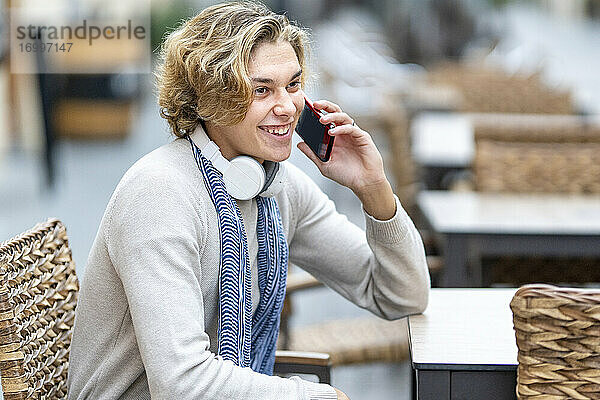 Mann lächelt  während er in einem Straßencafé mit seinem Handy telefoniert