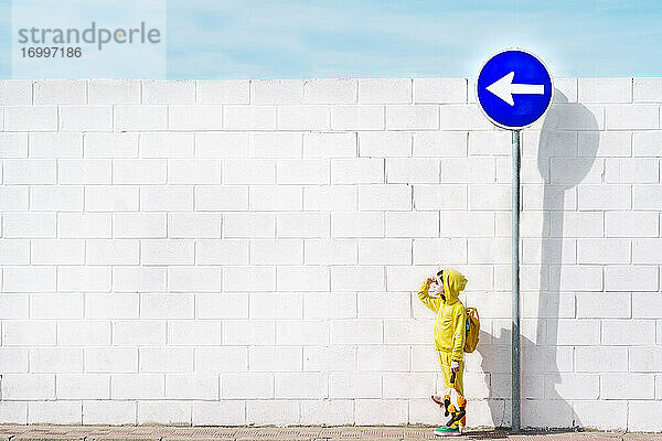 Mädchen mit ihrem Kuscheltier am Verkehrsschild  Richtung links  vor einer weißen Wand