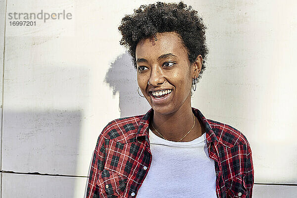 Lächelnde junge Afro-Frau  die gegen eine weiße Wand schaut