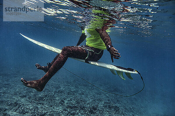 Männlicher Surfer auf dem Surfbrett sitzend in der Unterwasserwelt der Malediven