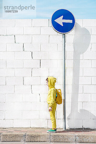 Mädchen stehend auf einem Verkehrsschild  Richtung links  vor einer weißen Wand