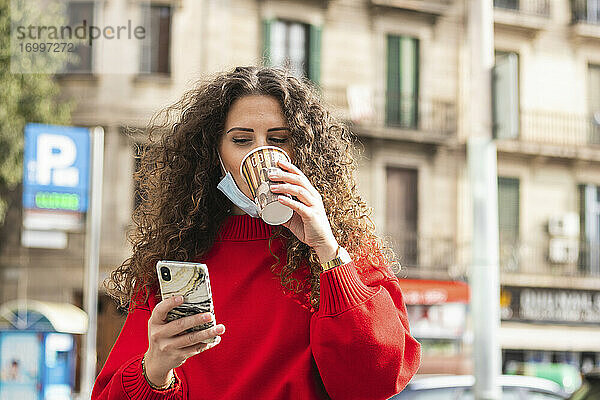 Geschäftsfrau  die ein Mobiltelefon benutzt  während sie während der COVID-19 einen Kaffee trinkt