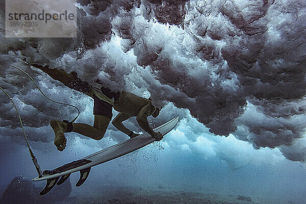 Männlicher Surfer auf dem Surfbrett beim Tauchen unter Wasser auf den Malediven