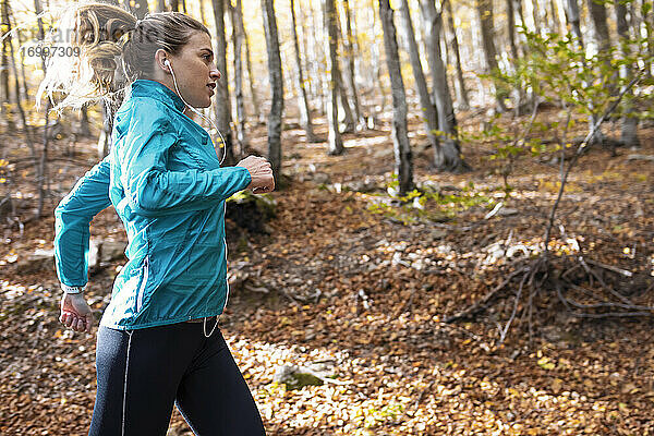 Sportlerin mit In-Ear-Kopfhörern hört Musik beim Laufen im Wald