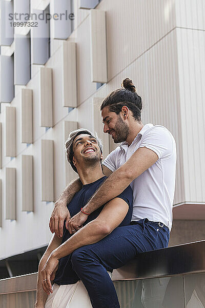 Lächelnder Mann  der seinen Partner ansieht  während er an einem Gebäude in der Stadt sitzt