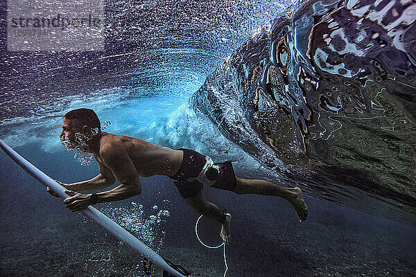 Männlicher Surfer taucht mit Surfbrett unter Wasser auf den Malediven