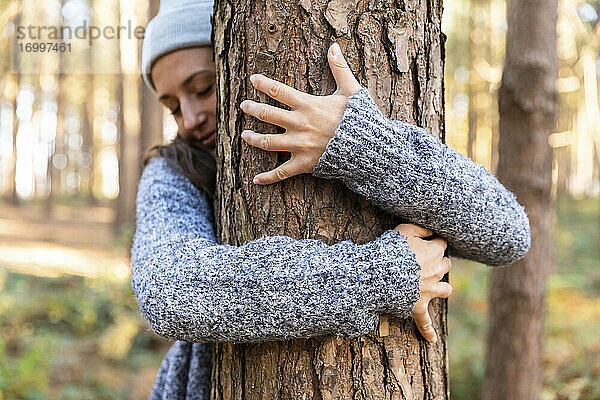 Weibliche Forscherin umarmt Baumstamm beim Wandern im Waldgebiet Cannock Chase