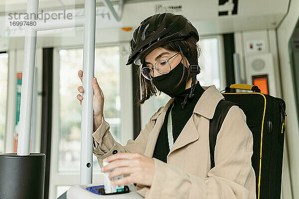 Frau mit Gesichtsmaske und Fahrradhelm  die eine Fahrkarte in der Straßenbahn entwertet