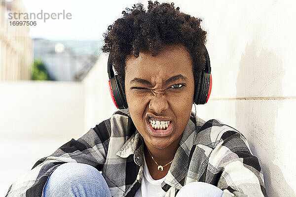 Afro junge Frau mit Grimasse im Gesicht hört Musik an der Wand